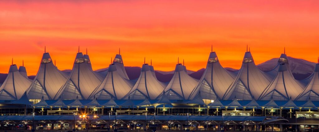 mrchauffeurcolorado | Stunning sunset over the iconic tent-like roofs of Denver International Airport, with vibrant orange skies and distant mountains in the background