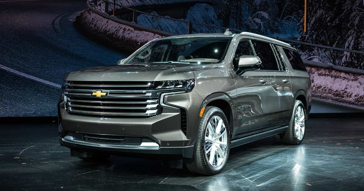 mrchauffeurcolorado | Sleek, metallic gray 2025 Chevrolet Suburban showcased on a dark stage, featuring modern design and premium features