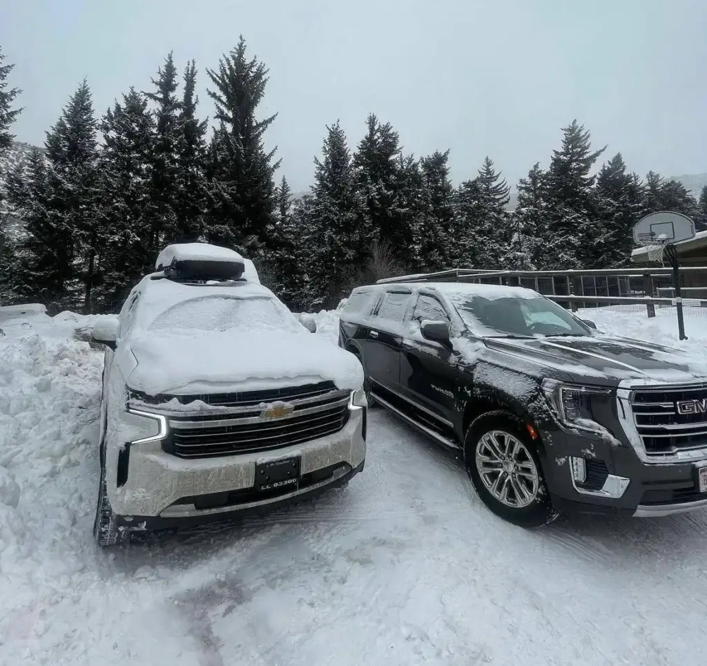 mrchauffeurcolorado | Two SUVs parked in a snowy landscape, each with a layer of snow on their roofs, creating a serene winter scene.