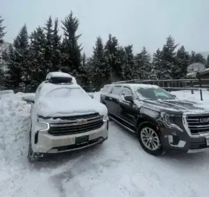 mrchauffeurcolorado | Two SUVs parked in a snowy landscape, each with a layer of snow on their roofs, creating a serene winter scene.