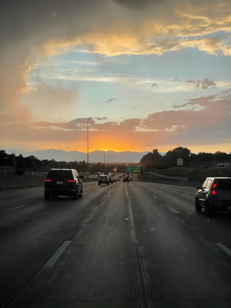 Scenic highway leading from Denver to Red Rocks Amphitheatre with stunning sunset over mountains.