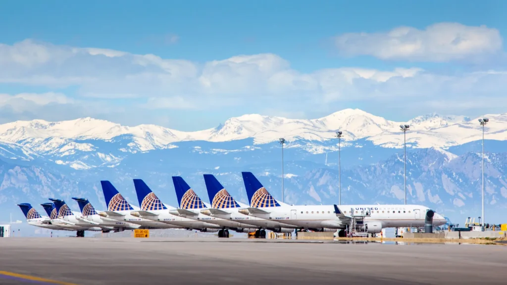 Line of United Express airplanes parked at an airport with snow-capped Colorado mountains in the background