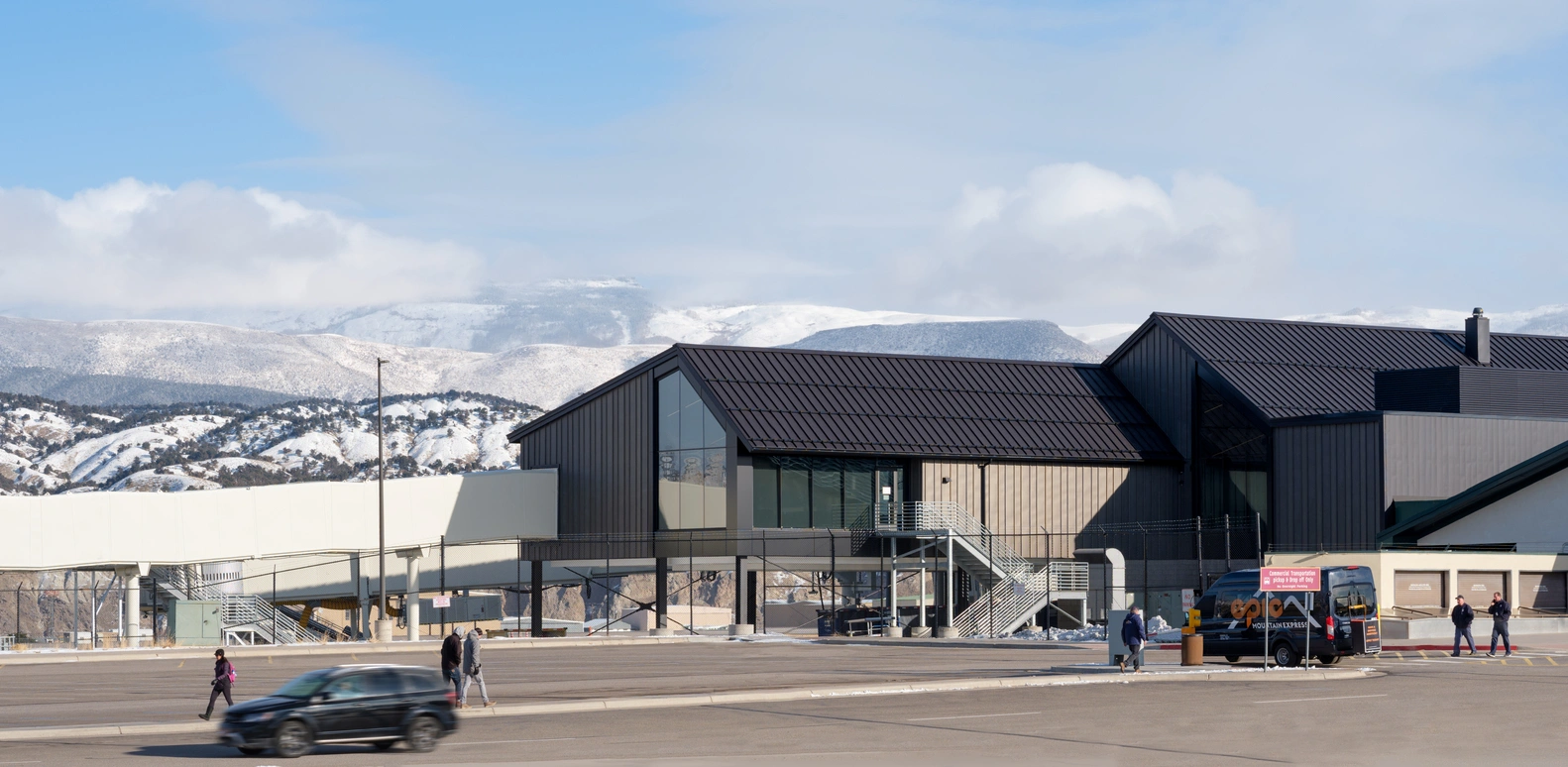 Eagle Airport terminal with a shuttle van and passengers on the curb, set against snow-dusted Colorado mountains - ideal for airport transfers and shuttle service