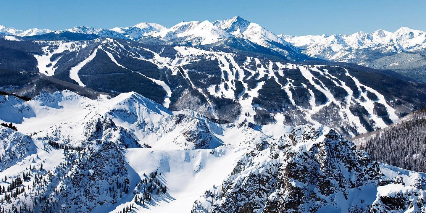 Aerial view of snow-covered mountain range with ski trails and slopes under a clear blue sky
