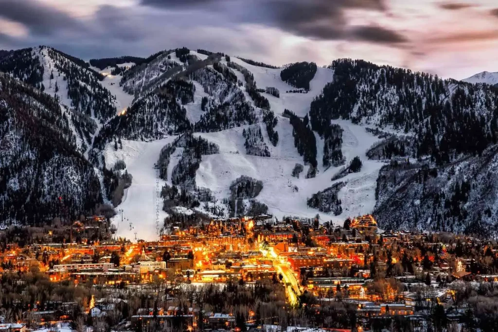 Stunning aerial view of Aspen, Colorado ski slopes and downtown lights at dusk, highlighting Mr. Chauffeur luxury transportation and shuttle service destination.