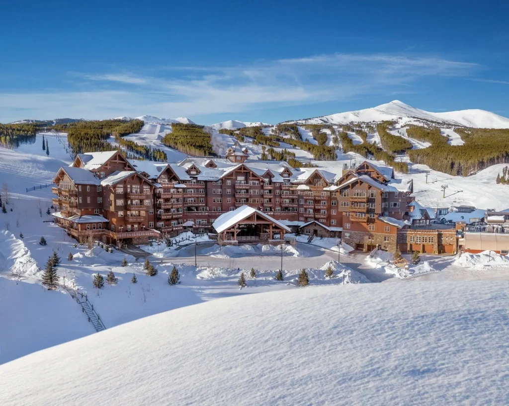 Ski-in/ski-out mountain lodge at Breckenridge Ski Resort, surrounded by groomed slopes, chairlifts, and pine forests beneath a clear blue sky
