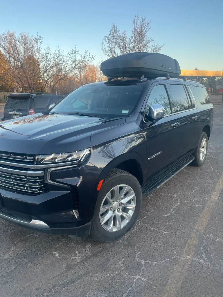 Side view of Mr. Chauffeur Colorado's black Chevy Suburban SUV with a roof cargo box, providing spacious luxury private car service for Denver airport transfers.