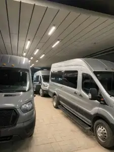 A row of gray passenger vans parked inside a covered garage with overhead lighting. Mr. Chauffeur Colorado Shuttle Service.