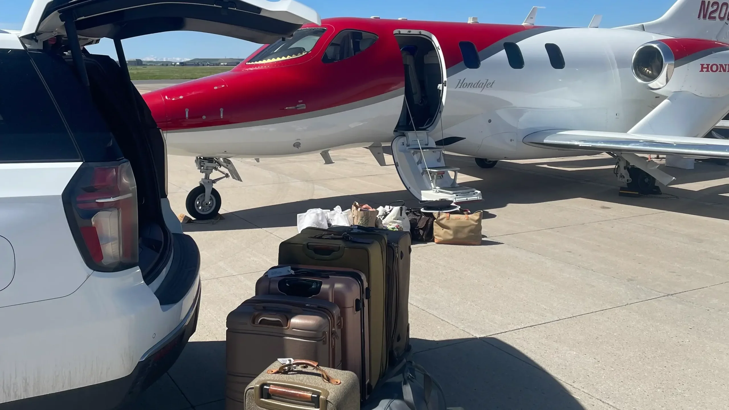 SUV with open trunk and stacked luggage beside a private jet on the airport tarmac under a clear blue sky, illustrating airport transfer and chauffeur service