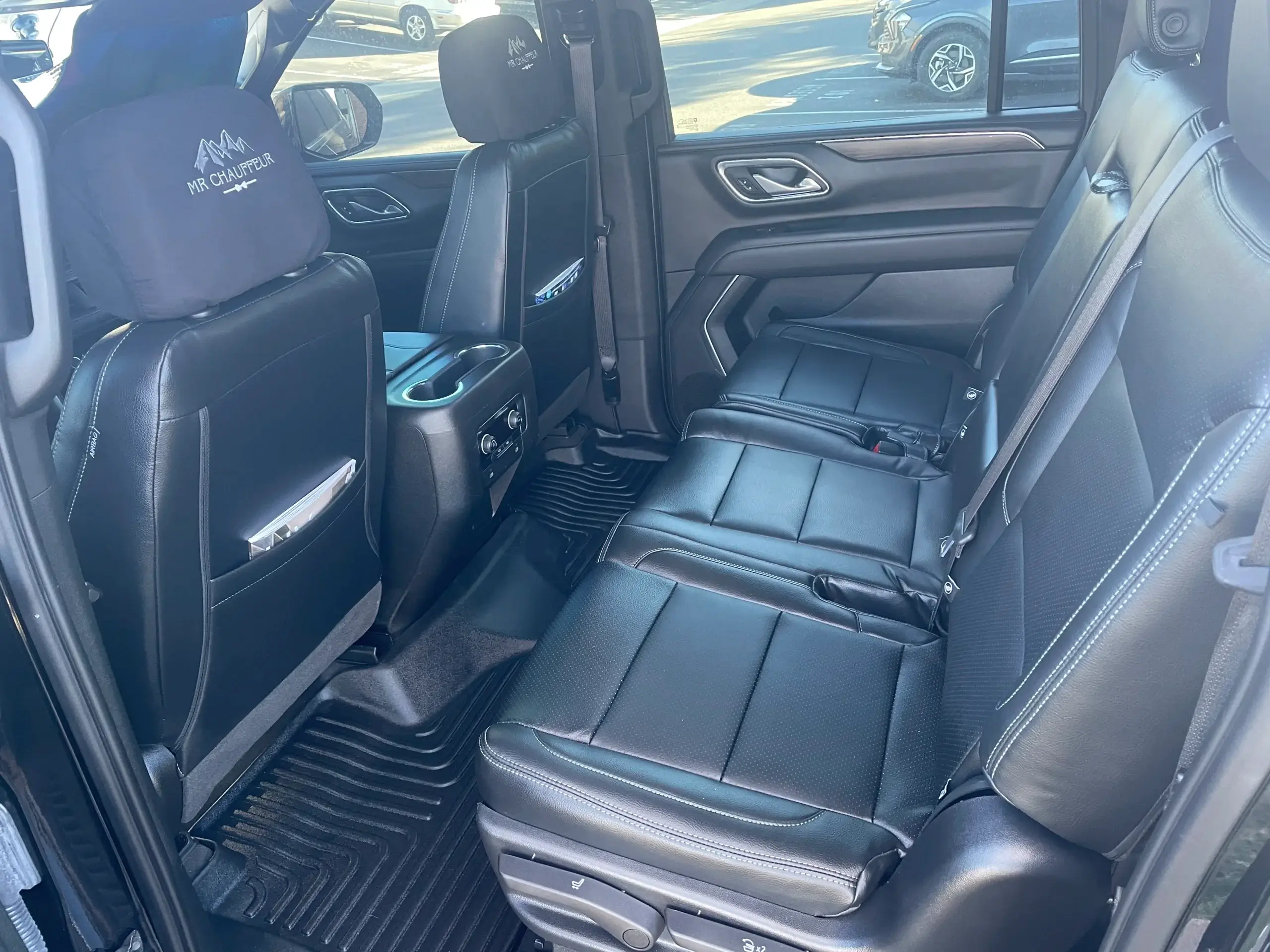 The interior passenger cabin of a Chevrolet SUV featuring a second-row black leather bench seat, black rubber floor mats, and front headrests with an embroidered "MR CHAUFFEUR" logo.
