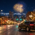 Denver skyline at night with New Year's Eve fireworks over the mountains and a private car waiting on the street